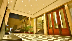 A hotel lobby with a checkered floor, a staircase, and a car parked outside. - Park Ascent (Noida)