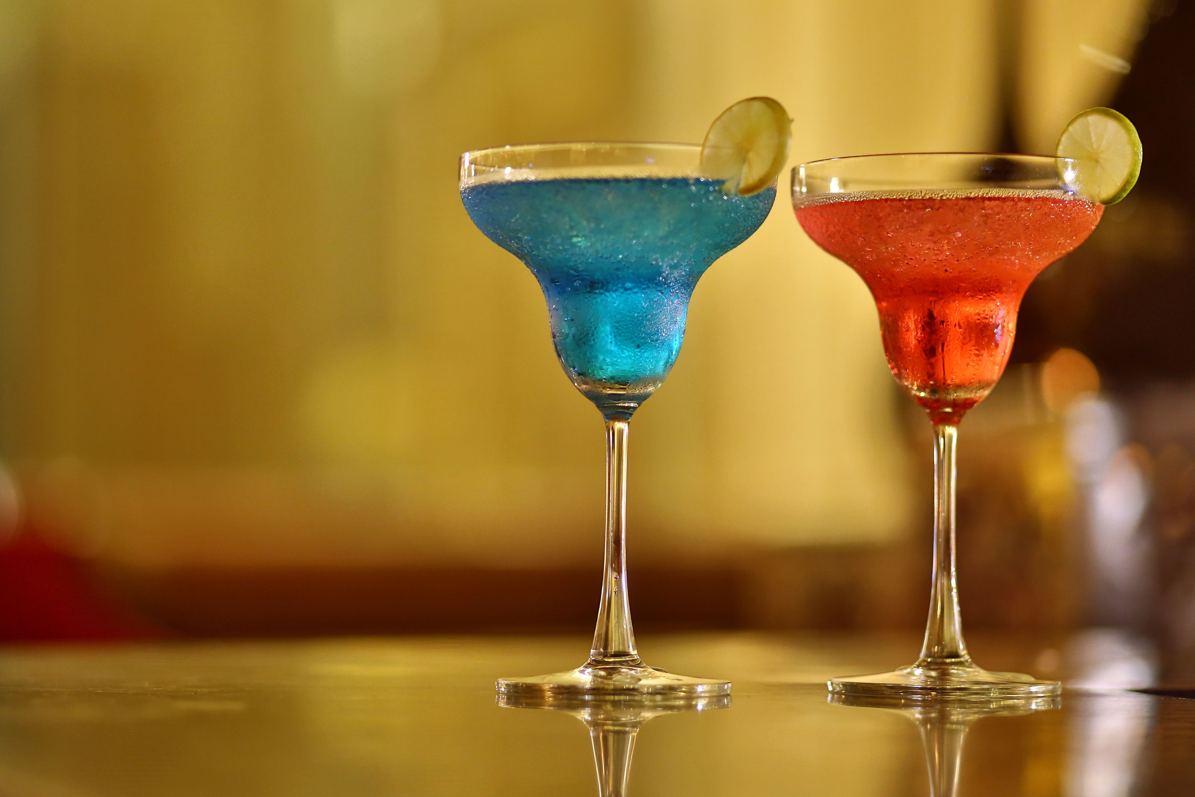 Two cocktails in martini glasses with lime garnishes on a reflective surface.