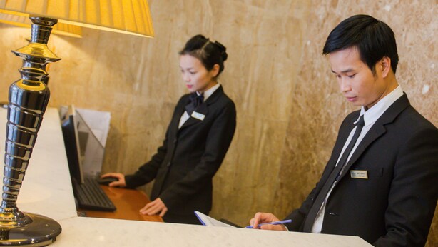 A reception desk with a lamp, a computer, and two staff members in formal attire. - Golden Art Hotel (Hanoi)