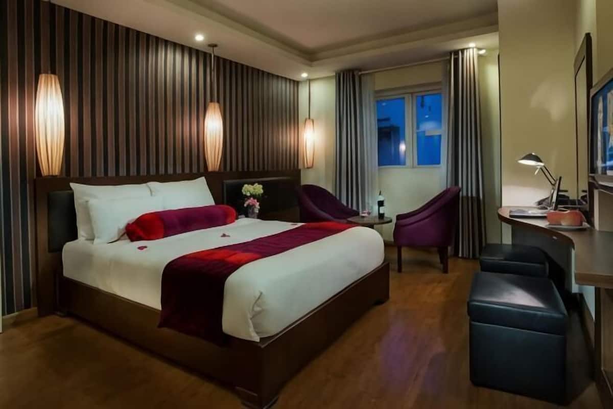A hotel room with a large bed, a desk, a chair, and a window with curtains.