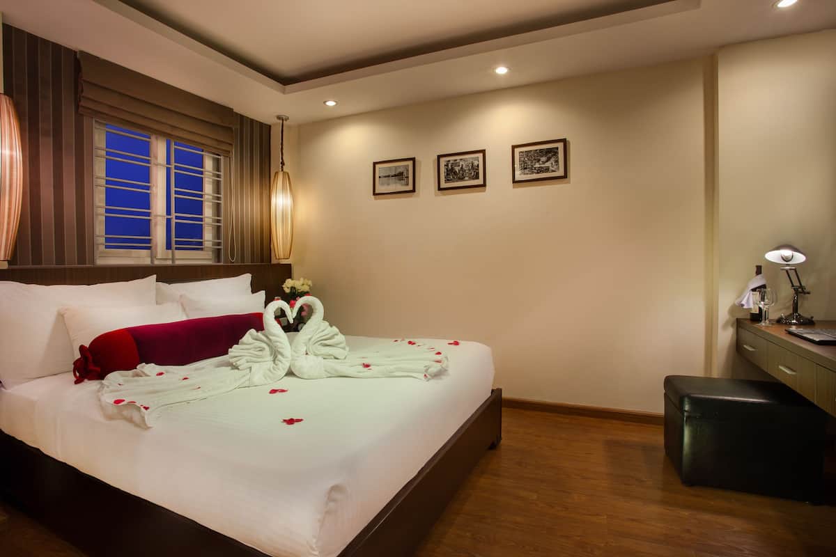 A hotel room with a large bed, a desk with a lamp, and three framed pictures on the wall.
