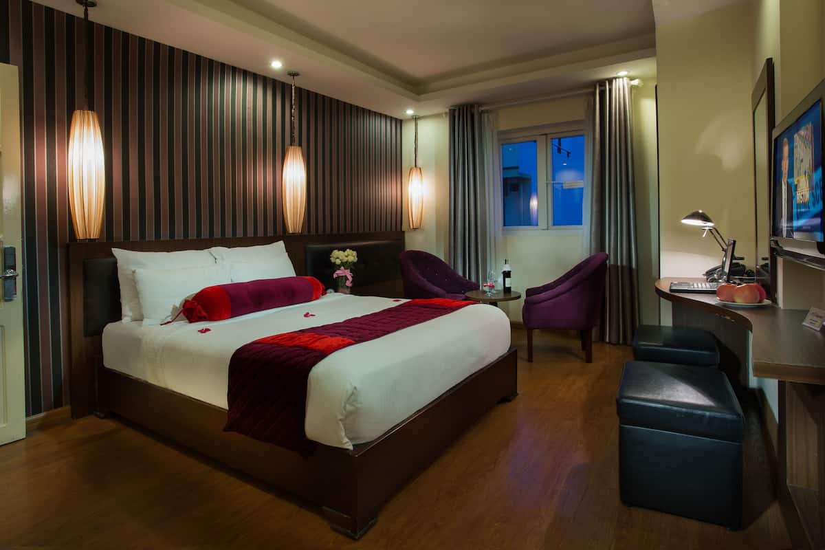 A hotel room with a large bed, a desk with a chair, a TV, and a window with curtains.