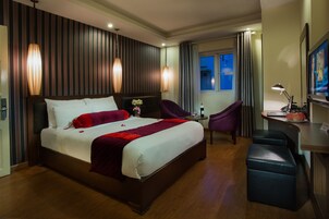 Habitación de hotel con una cama grande, un escritorio con silla, televisión y ventana con cortinas.