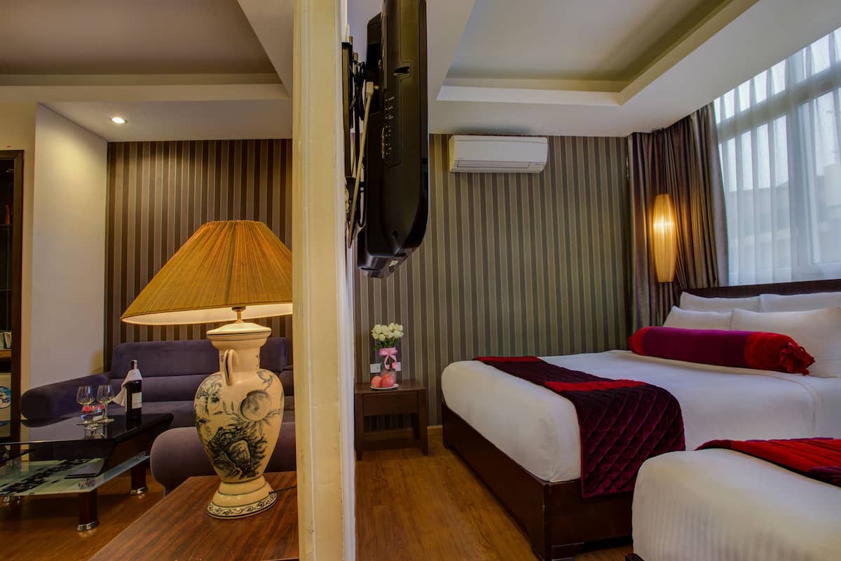 A hotel room with a bed, a sofa, a lamp, a TV, and a small table with a bottle and glasses.