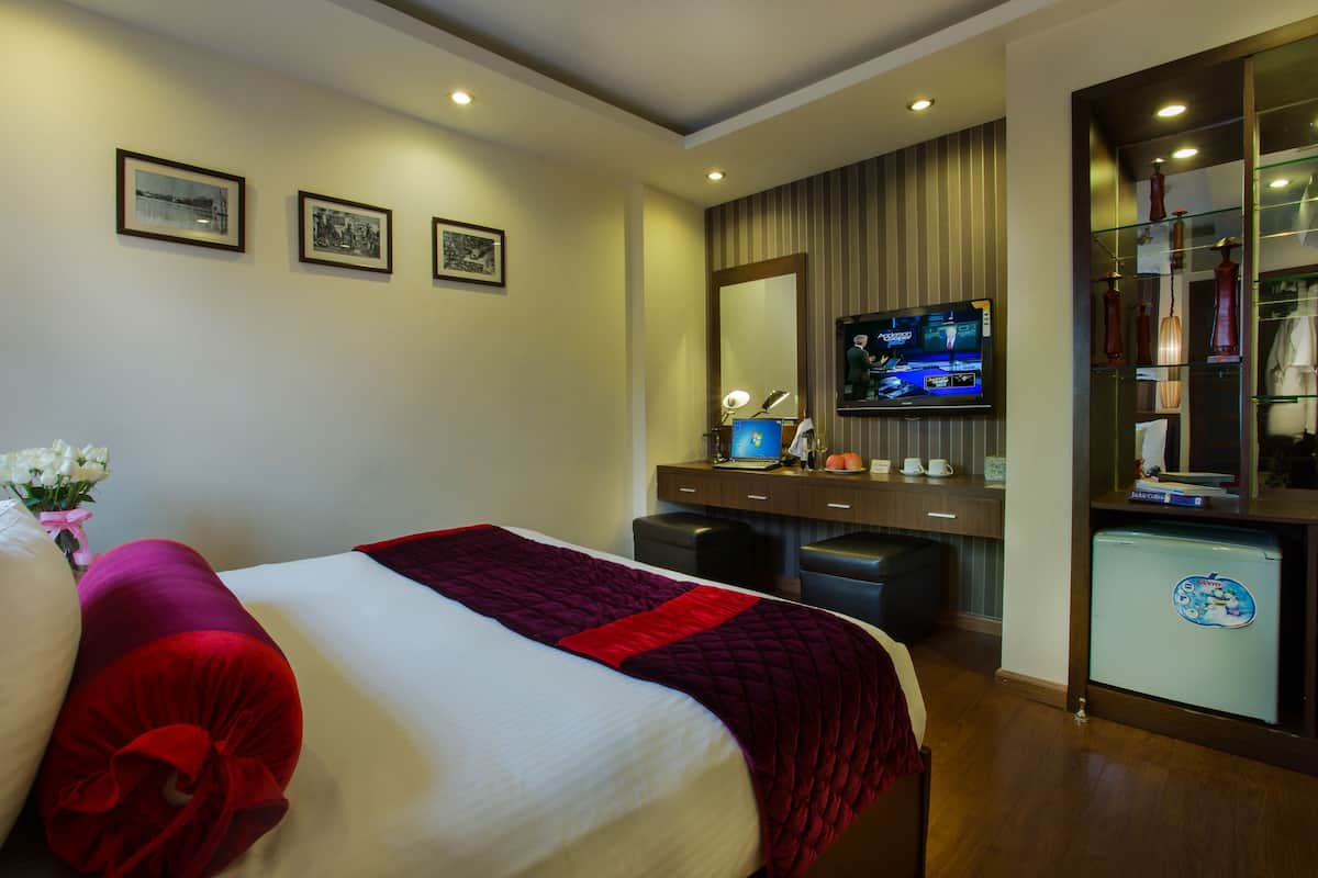 A hotel room with a large bed, a desk with a computer, a television, and a minibar.