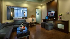 A modern living room with a sofa, ottoman, coffee table, and a television. - Golden Art Hotel (Hanoi)