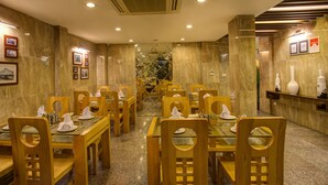 A restaurant with marble walls, wooden tables and chairs, and framed pictures on the walls. - Golden Art Hotel (Hanoi)