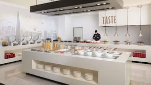 A modern kitchen with a cityscape mural, a central island with food items, and a chef preparing food. - ibis Ambassador Seoul Insadong (Seoul)
