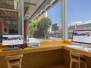 Ein Arbeitsplatz mit zwei Computern, einem Drucker und einem Fenster mit Blick auf die Straße.