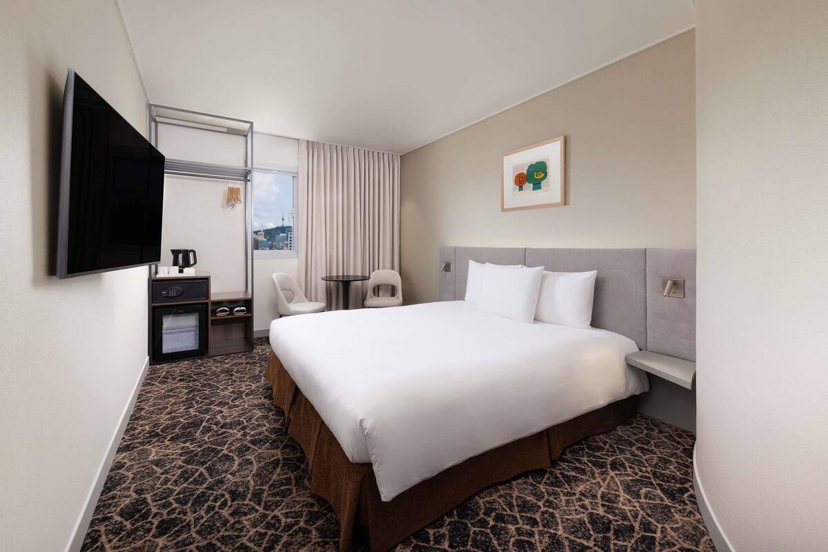 Ein Hotelzimmer mit einem großen Bett, einem Flachbildfernseher, einer Kaffeemaschine, einem kleinen Tisch und Blick auf die Stadt.