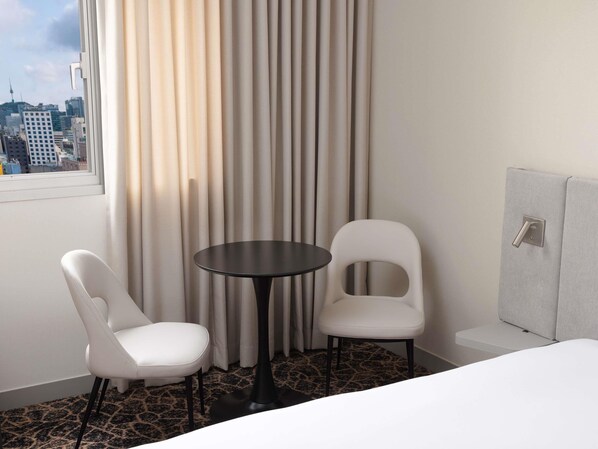 Une chambre d’hôtel avec un lit, deux chaises, une petite table, une fenêtre avec des rideaux et une vue sur la ville.