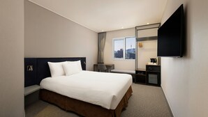 Une chambre d’hôtel équipée d’un lit, d’un bureau, d’une chaise, d’une télévision et d’une fenêtre donnant sur la ville.