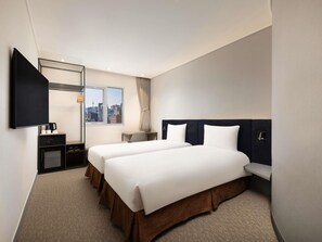 Ein Hotelzimmer mit zwei Betten, einem Fernseher, einem Schreibtisch mit Kaffeemaschine und einem Fenster mit Blick auf die Stadt.