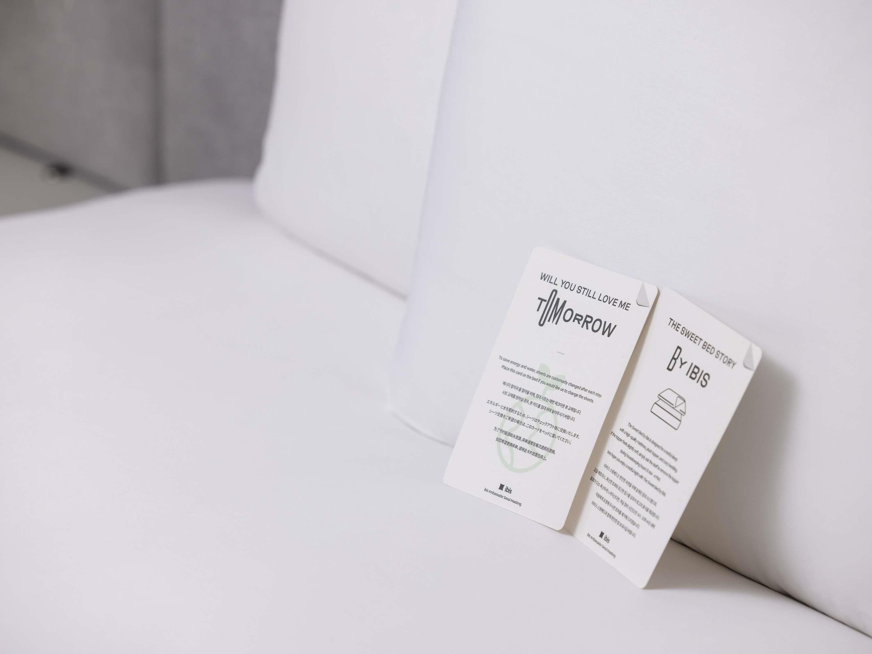 Two white cards on a white sofa. One card reads 'WILL YOU STILL LOVE ME TOMORROW' and the other 'THE SWEET BED STORY BY IBIS'.