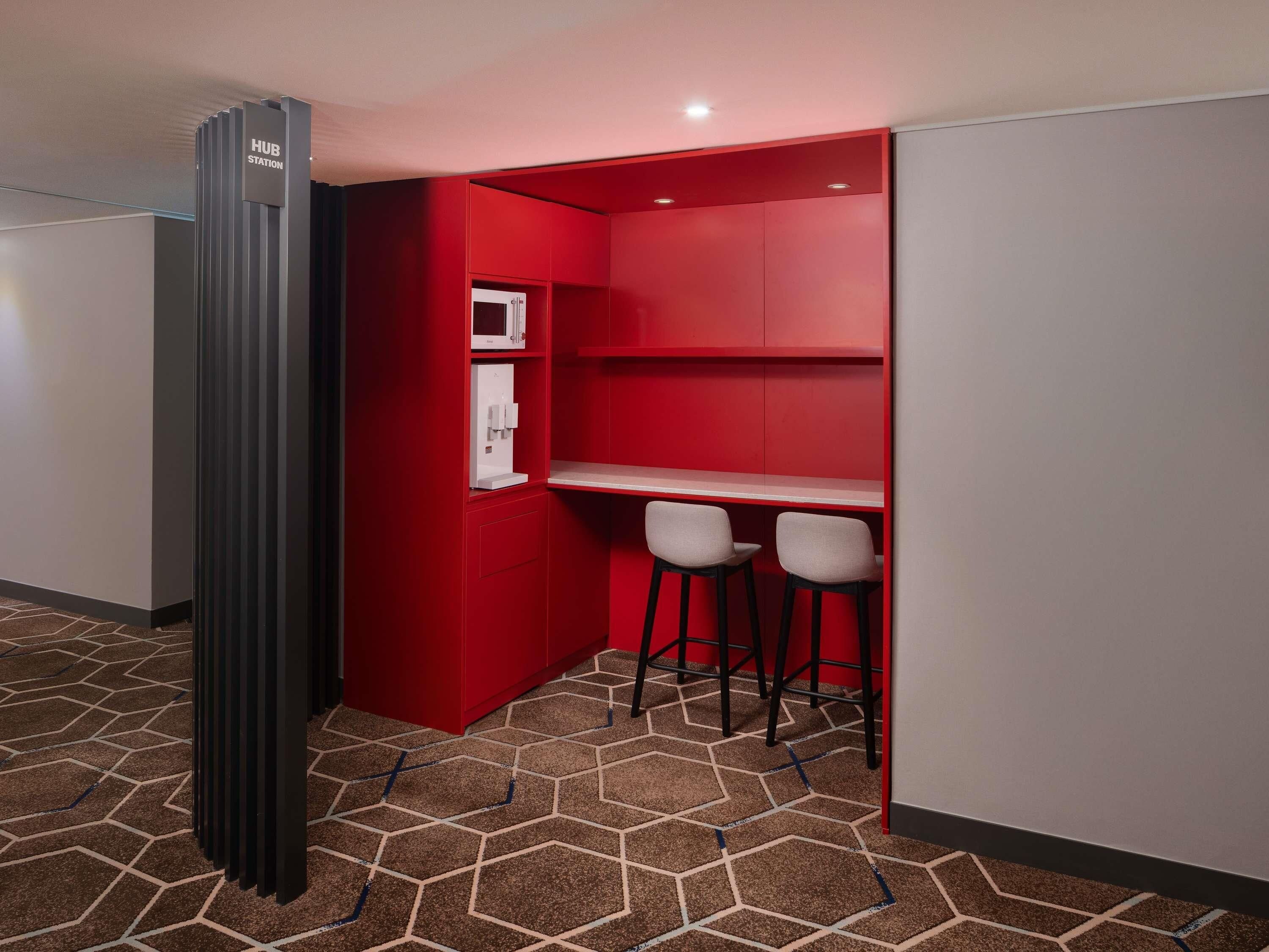 A compact room with a red accent wall, a microwave, a power outlet, and two bar stools.