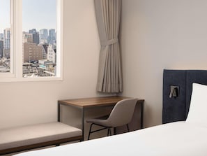 Ett hotellrum med en säng, ett skrivbord, en stol, utsikt över stadsbilden och en gardin.