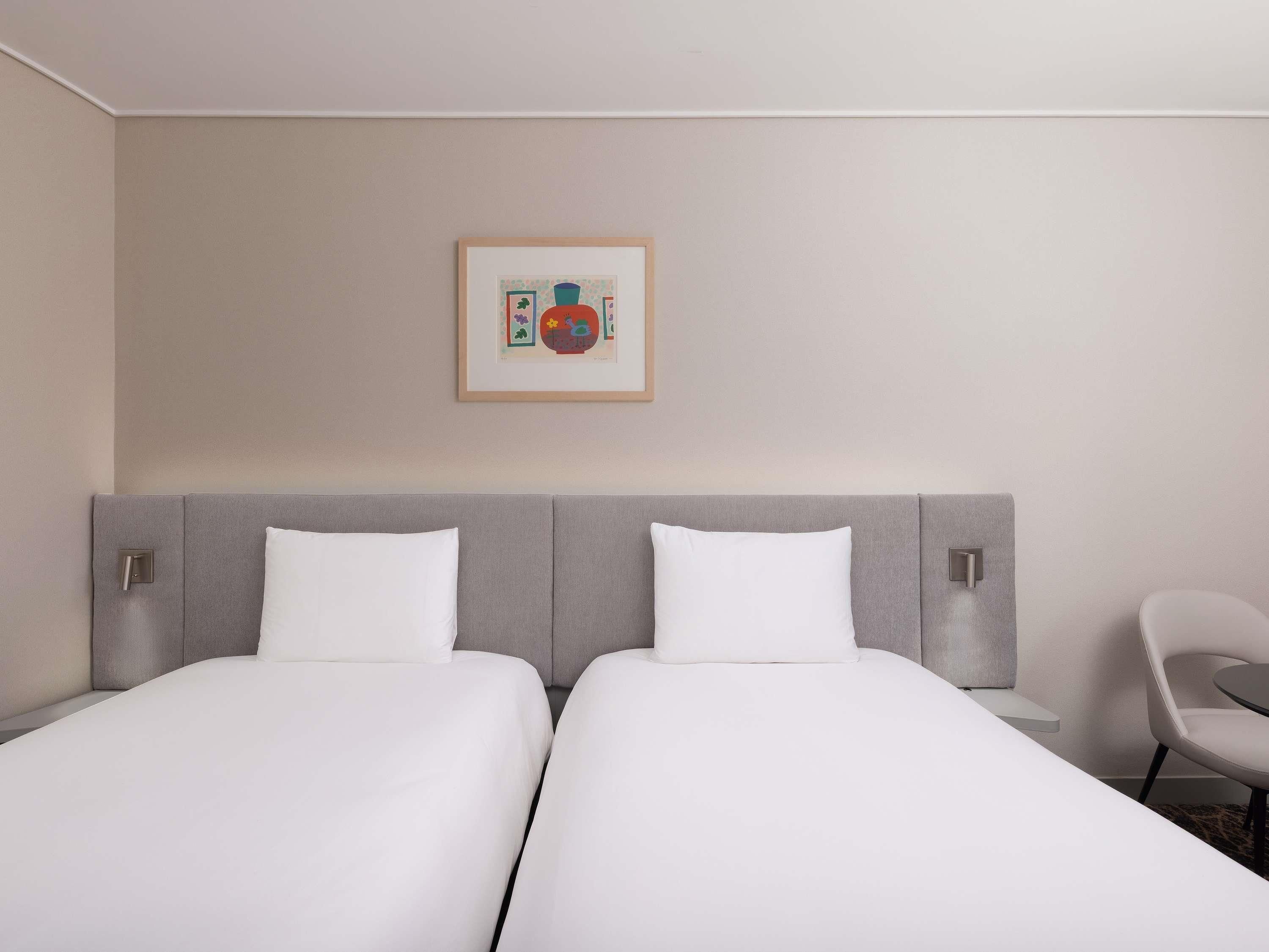 A hotel room with two beds, a framed picture on the wall, and a chair.