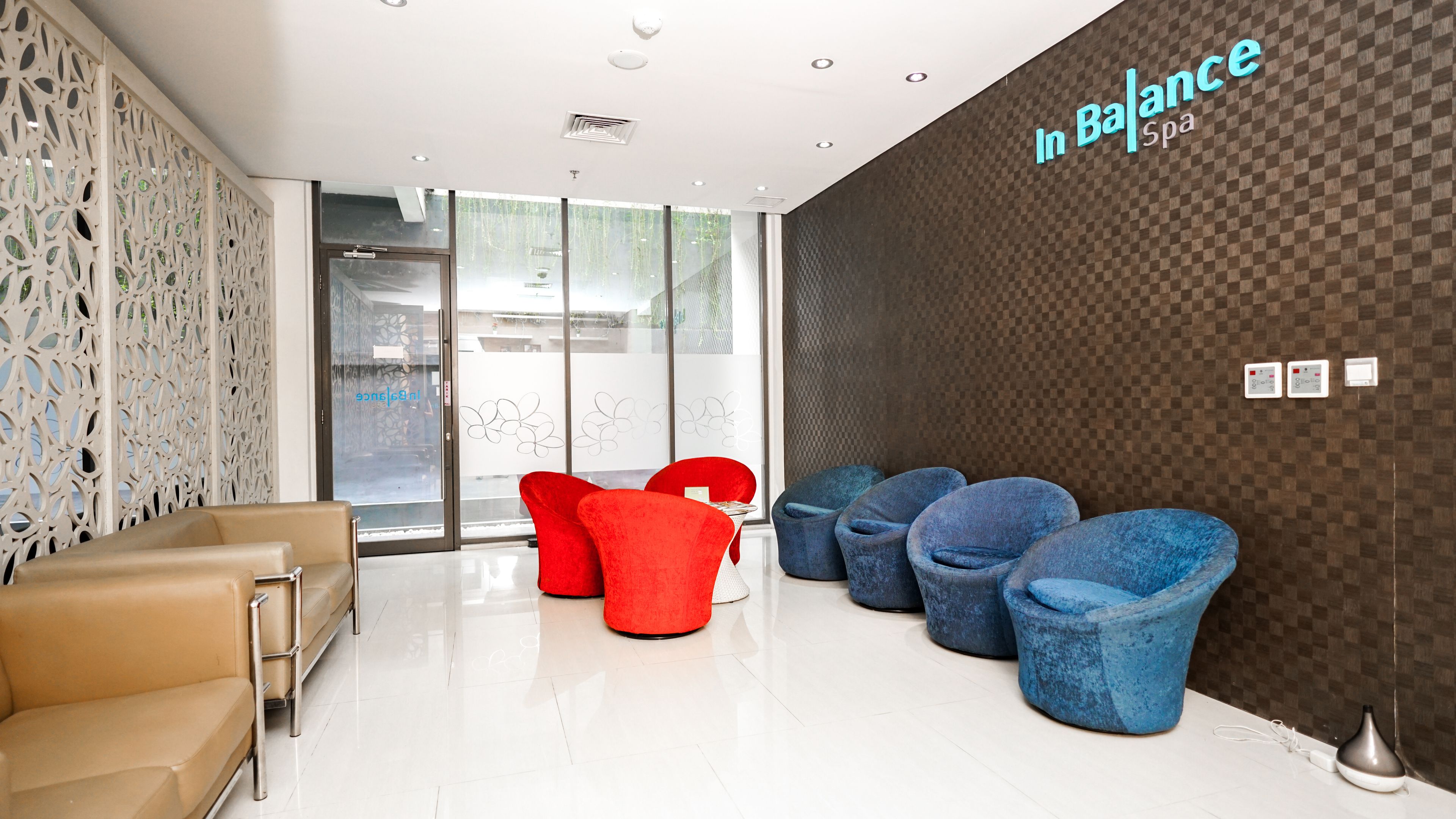 A modern waiting area with beige sofas, red and blue chairs, and a checkered wall with 'In Balance spa' signage.