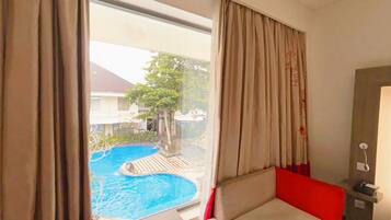 Habitación de hotel con vista a una piscina, una cama y una mesita de noche con una lámpara.