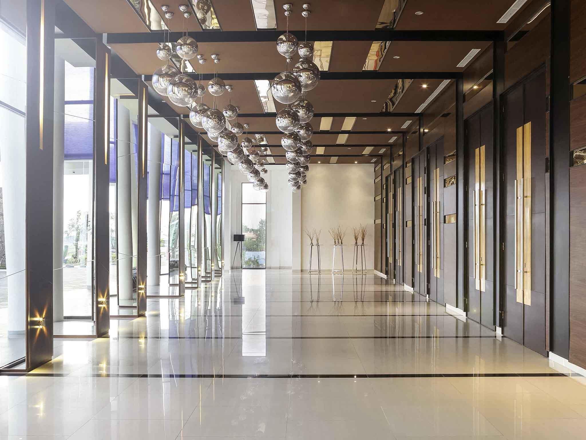A modern interior with reflective floors, a central hanging light fixture, and a view through a glass door.