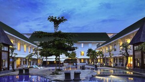 A hotel courtyard with a central pool, surrounded by buildings with balconies and outdoor seating areas. - Hotel Novotel Banjarmasin Airport (Banjarbaru)