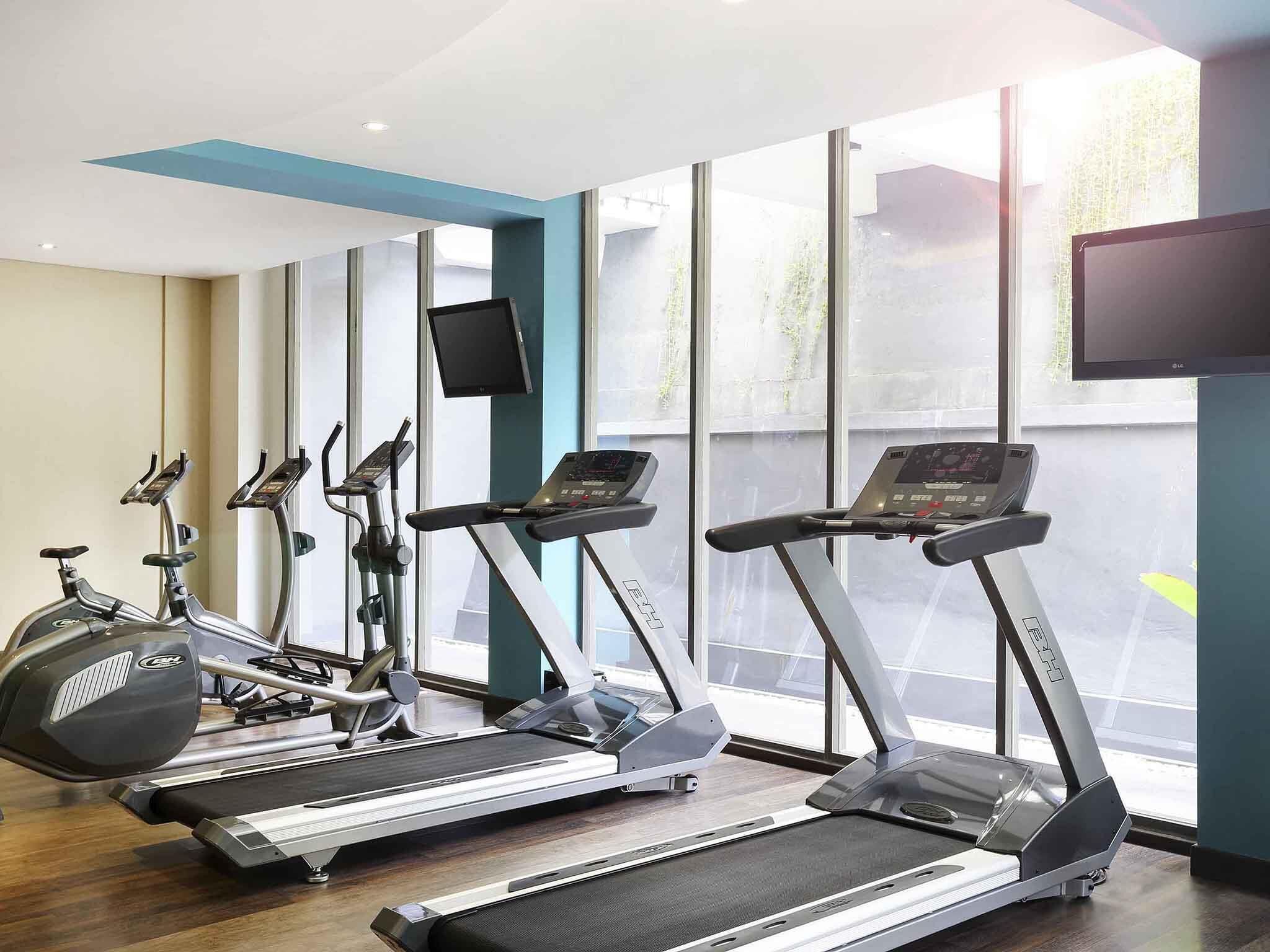 A gym with treadmills, stationary bikes, and a TV screen.