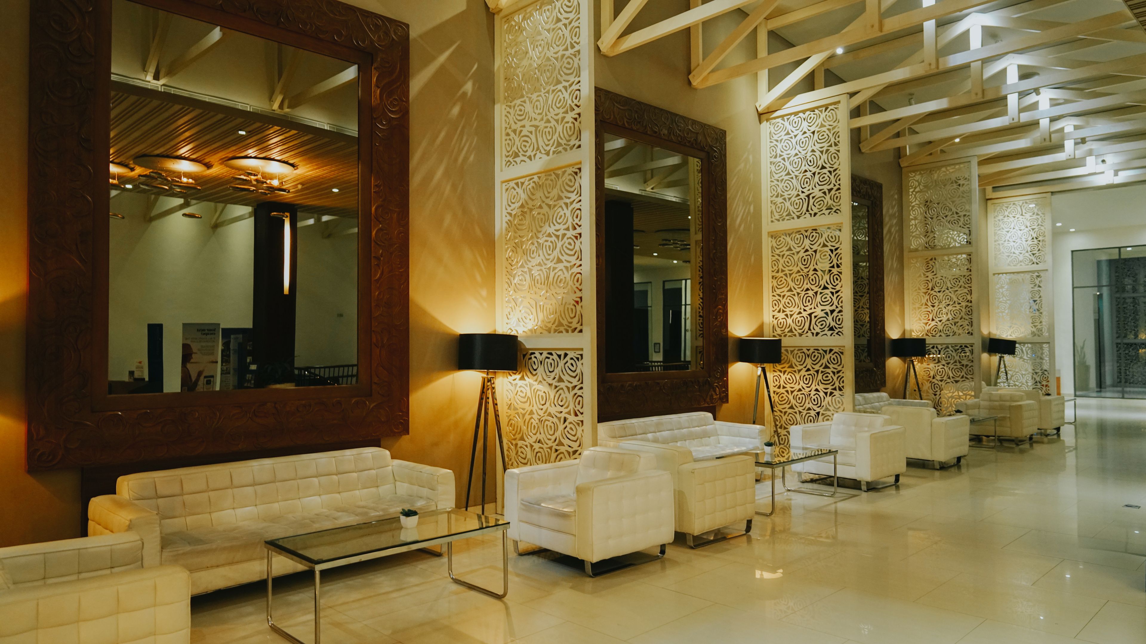 A spacious lobby with white sofas, a glass coffee table, and large mirrors.