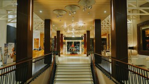 A hotel lobby with a staircase, wooden columns, and a reception desk. - Hotel Novotel Banjarmasin Airport (Banjarbaru)