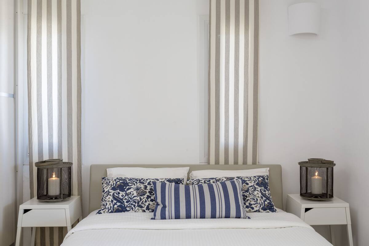 Une chambre à coucher bien rangée, avec un lit, deux tables de chevet et deux lampes fixées au mur.