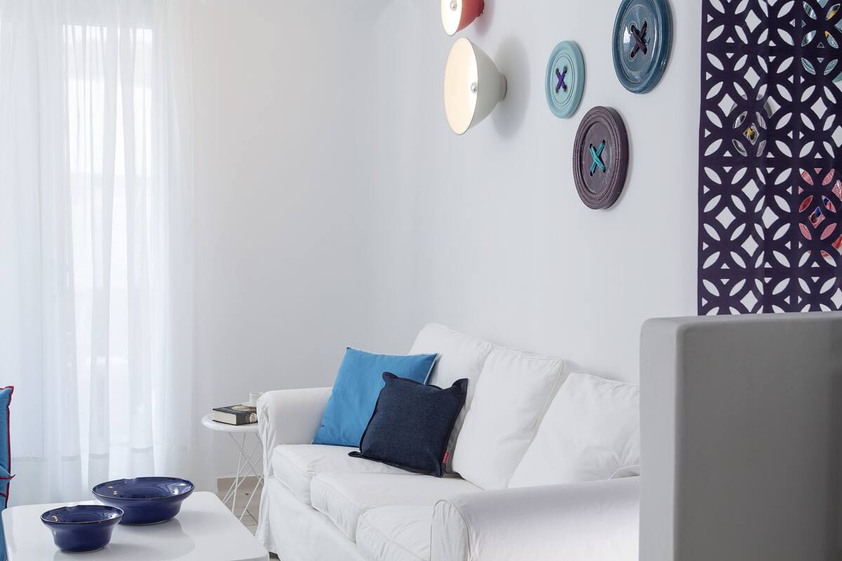 Un salon moderne avec un canapé blanc, des coussins bleus et marine, des assiettes décoratives accrochées au mur et un panneau décoratif à motifs.