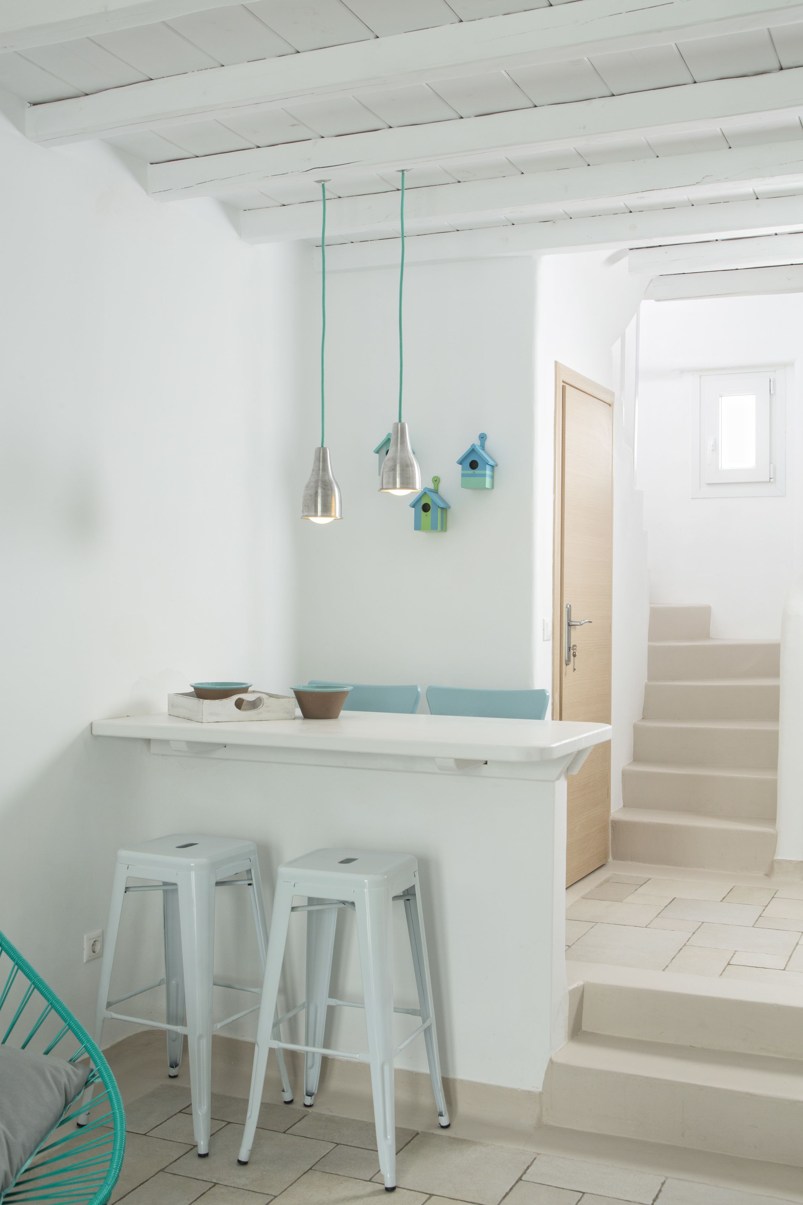 A kitchen with white bar stools, a white countertop, and hanging pendant lights.