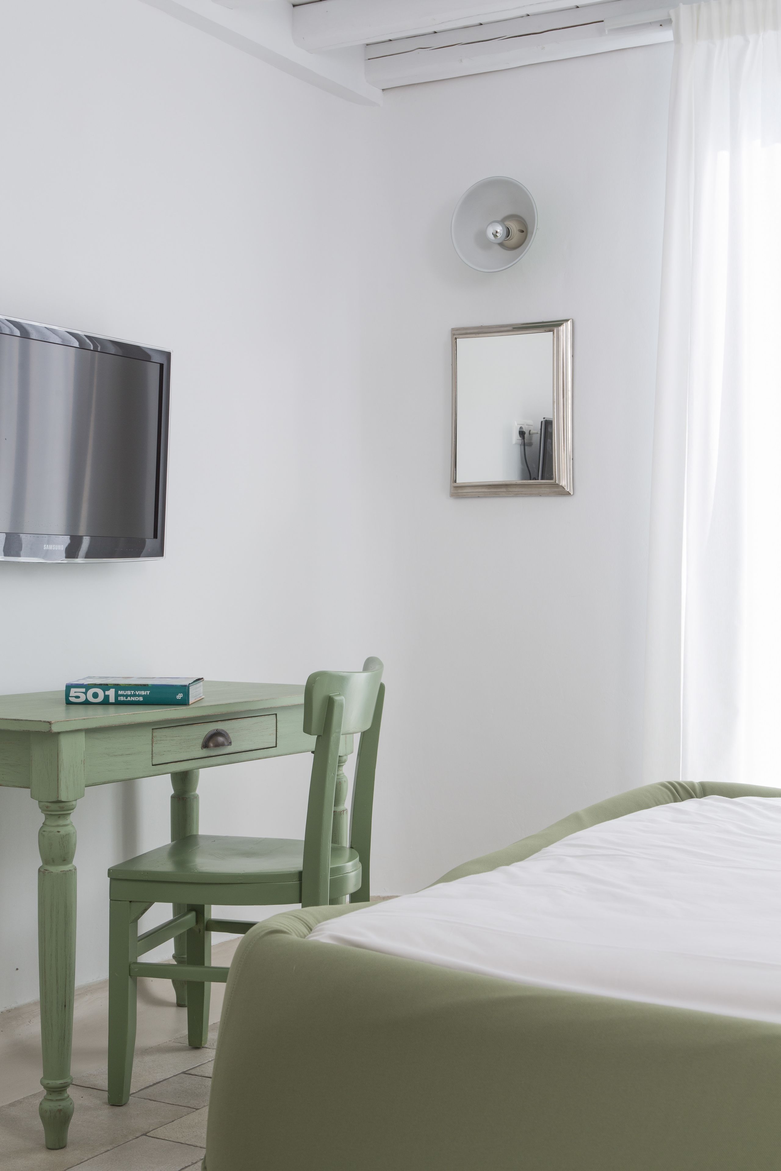 A room with a bed, a desk with a chair, a television, a mirror, and a light fixture.