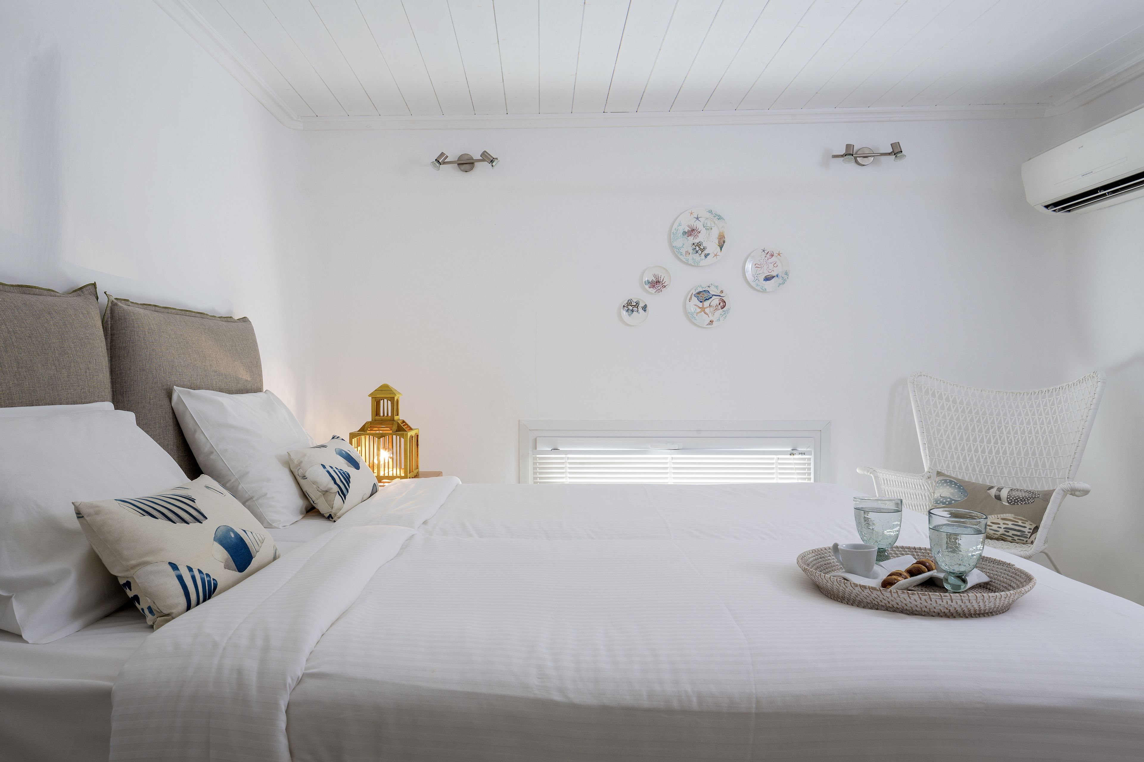 A bedroom with a neatly made bed, a bedside table with a lamp, and a tray with glasses and snacks.