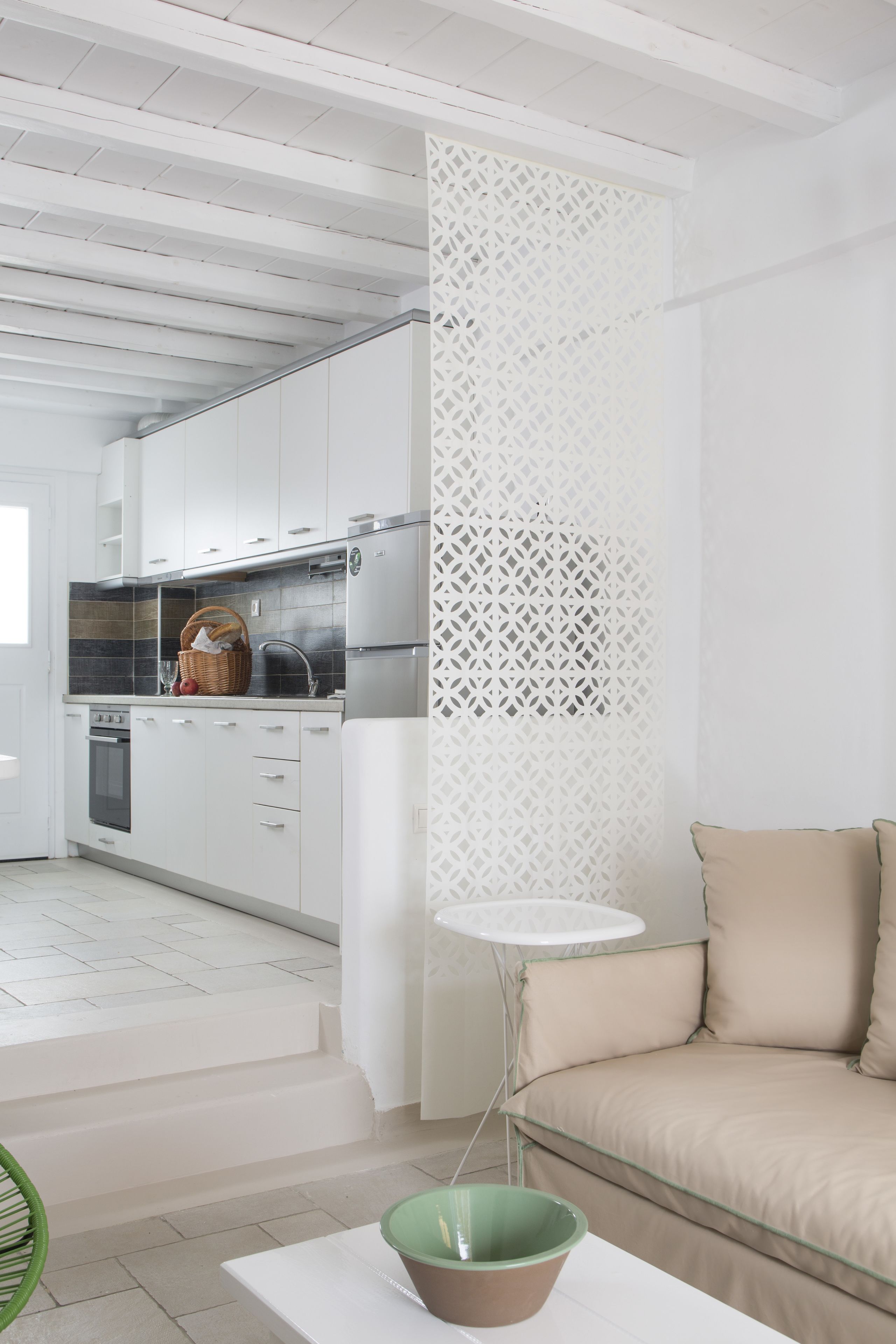 Una cocina moderna con armarios blancos, horno integrado y refrigerador. Hay una cesta de mimbre en la encimera y un tazón verde sobre una mesa blanca.