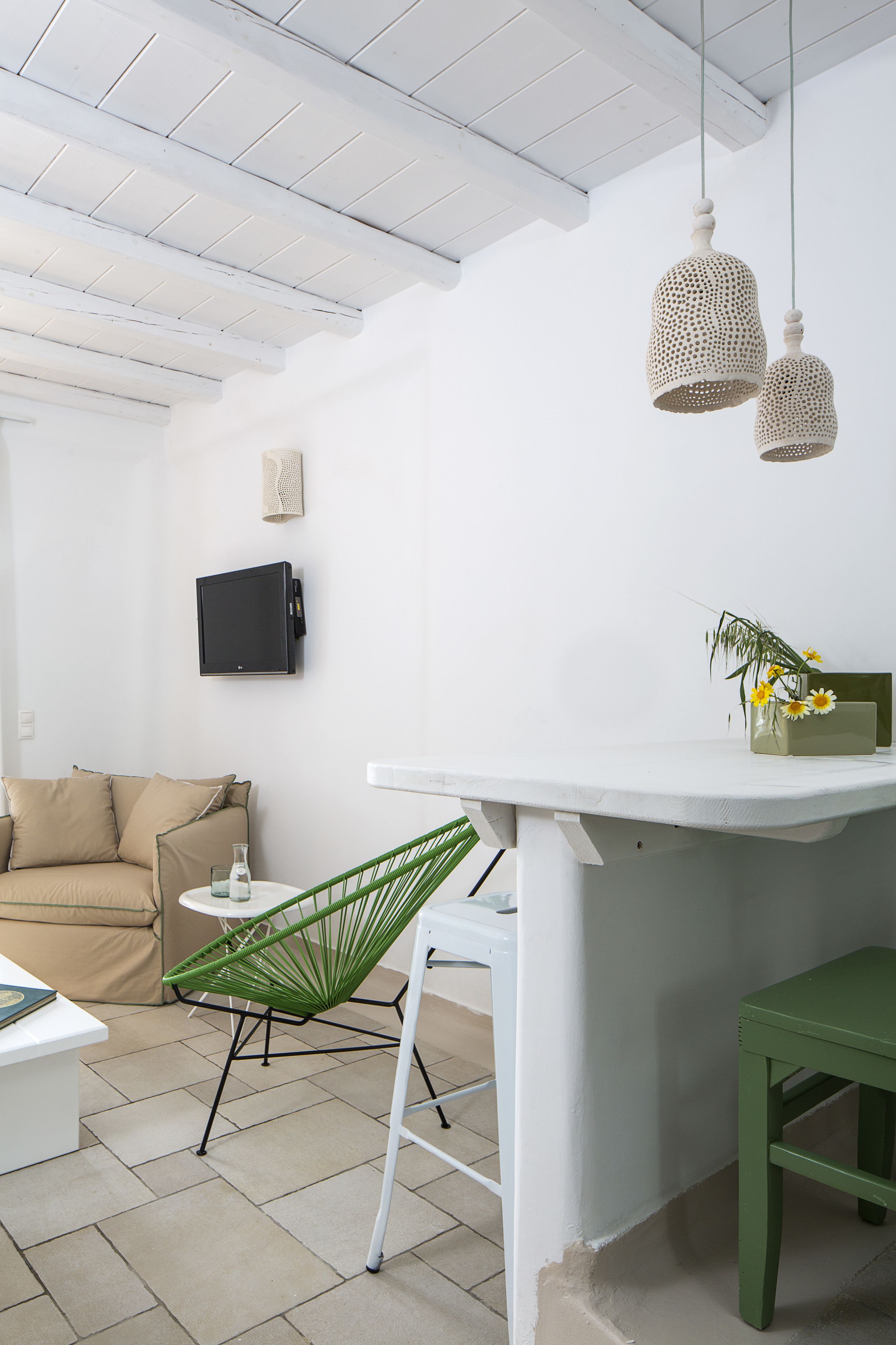 Ein zeitgemäßer Wohnraum mit einem weißen Sofa, einem grünen Sessel, einem kleinen Tisch und einem weißen Beistelltisch mit Blumen in einer Vase.