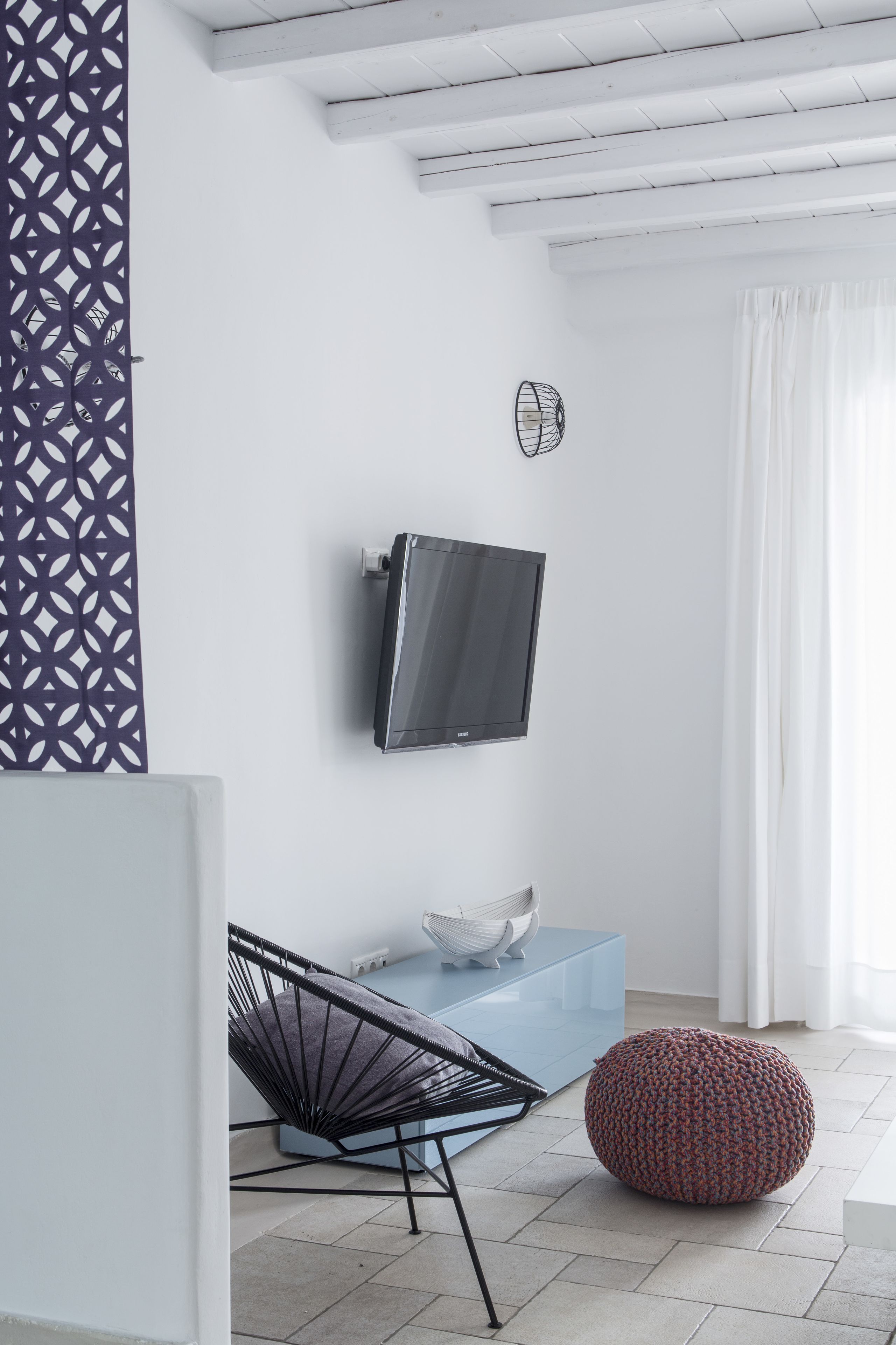 Una sala de estar moderna con un televisor montado en la pared, un sofá azul, un sillón negro y un otoman redonda.