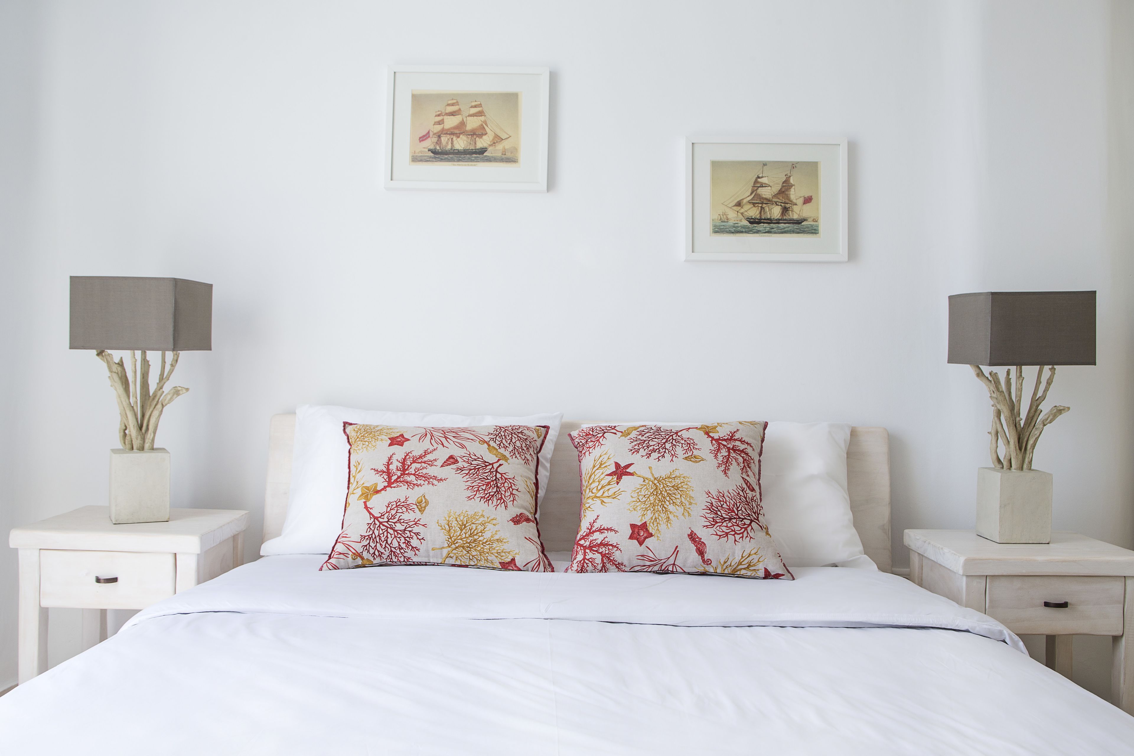 A neatly made bed with white bedding, two matching pillows, a bedside table with a lamp, and two framed pictures on the wall.