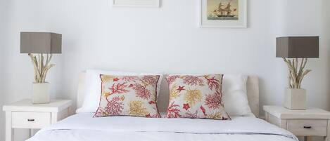 A neatly made bed with white bedding, two matching pillows, a bedside table with a lamp, and two framed pictures on the wall.