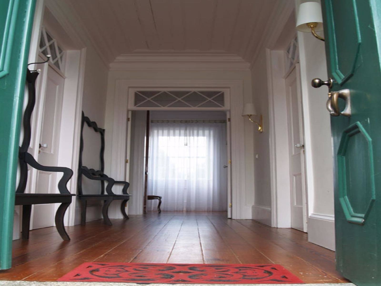Un pasillo con suelo de madera, un tapete rojo y una puerta con marco verde.