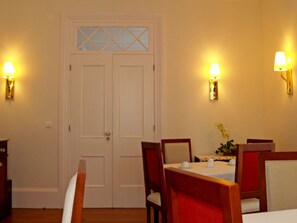 Un comedor con una puerta blanca, dos lámparas de pared y una mesa dispuesta para dos personas.