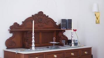 Uma cômoda de madeira com tampos de mármore, duas velas, uma pequena mesa com castiçal e um abajur fixado na parede.