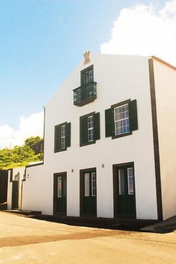 Un edificio blanco con contraventanas negras y un balcón.
