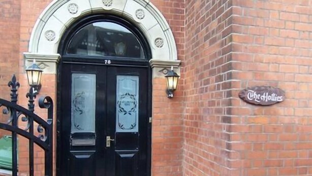 A black double door with a number '76' above it, set in a brick building with a sign reading 'The Hollies'. - The Hollies (Bridlington)