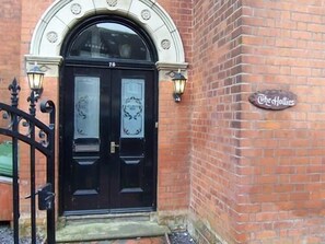 A black double door with a number '76' above it, set in a brick building with a sign reading 'The Hollies'. - The Hollies (Bridlington)