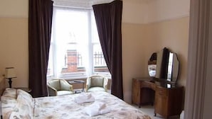 A hotel room with a large bed, a desk, a chair, and a window with curtains. - The Hollies (Bridlington)