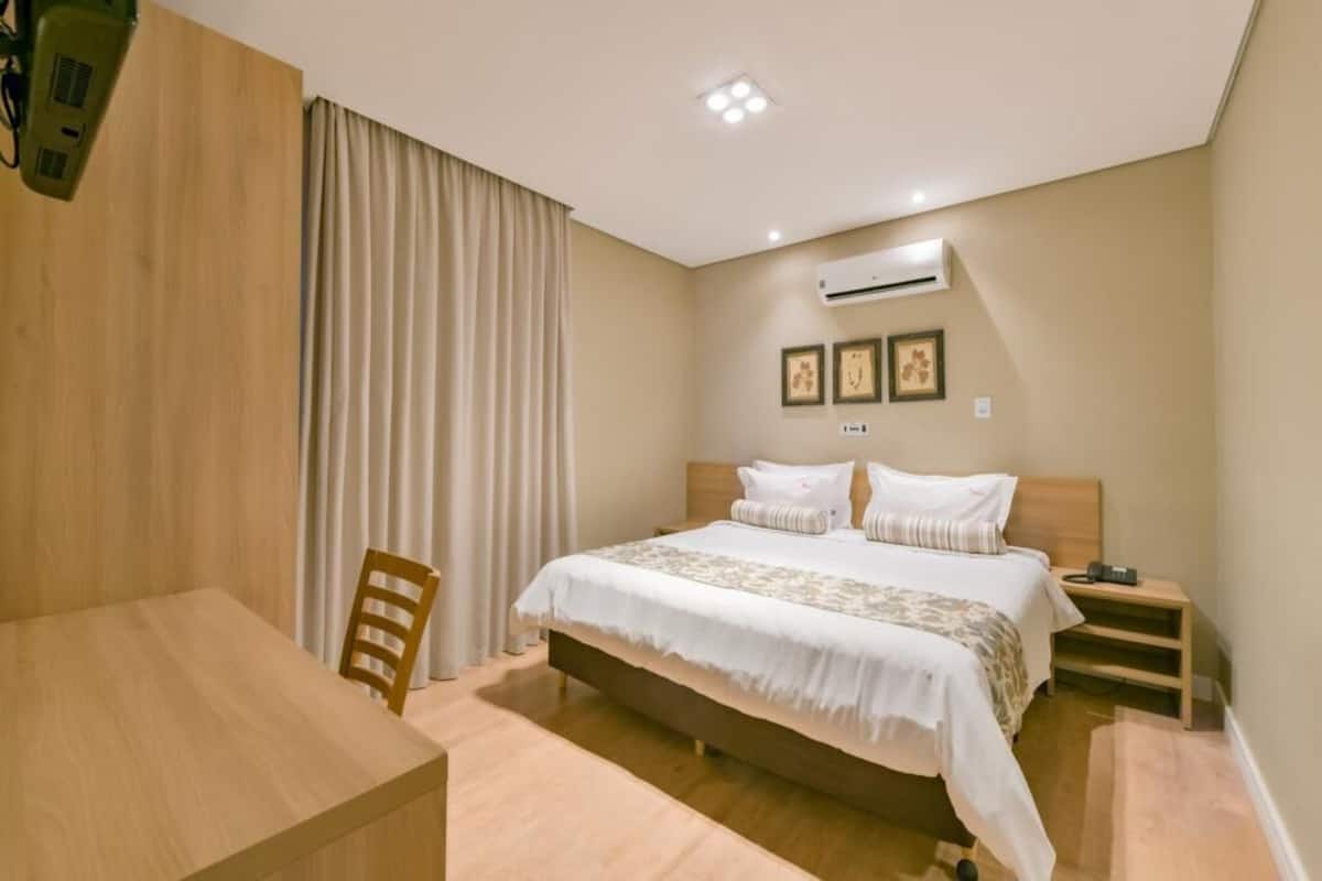 A bedroom with a bed, bedside table, chair, and an air conditioning unit.