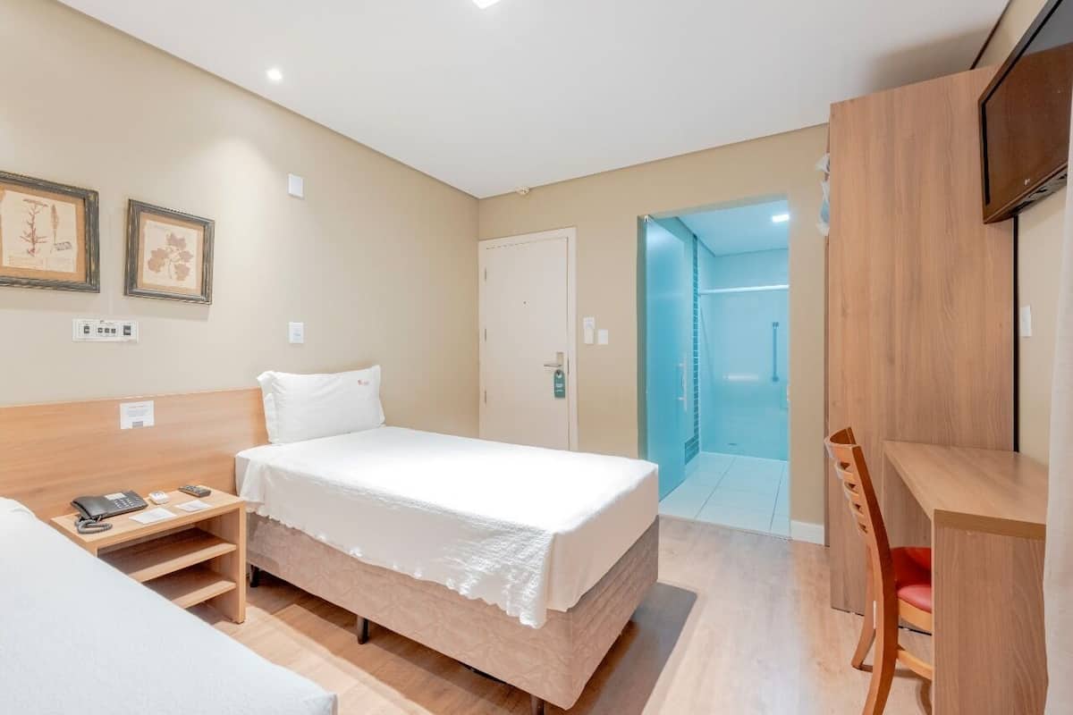 A hotel room with a bed, a desk, and a chair. There is a door leading to a bathroom.