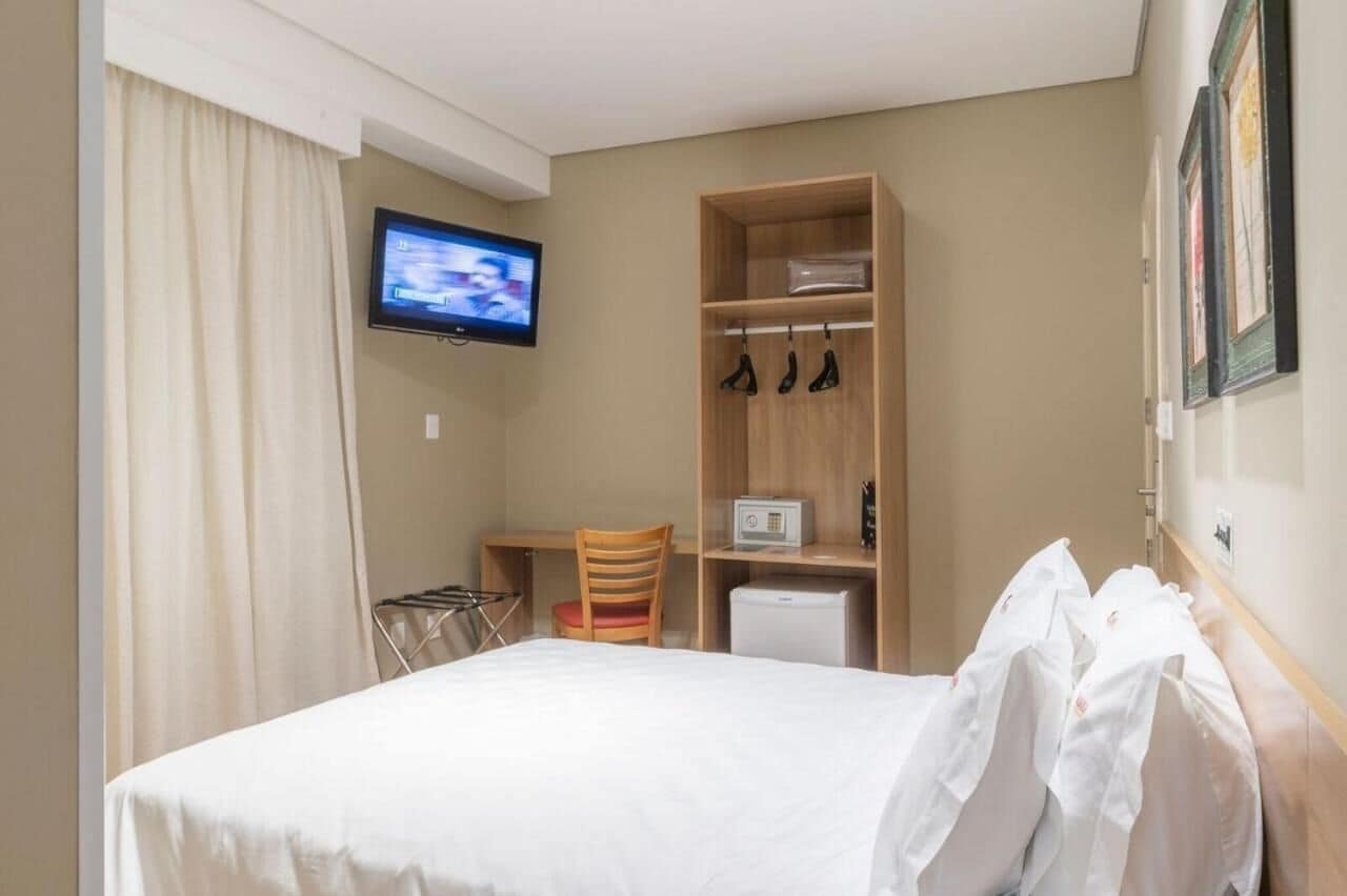 A hotel room with a bed, a desk, a chair, a TV, and a wardrobe.