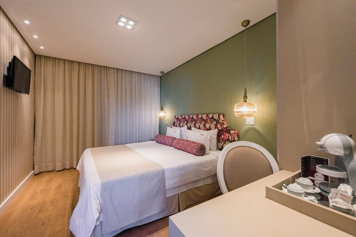 A hotel room with a bed, a desk, a chair, a television, and a coffee machine.