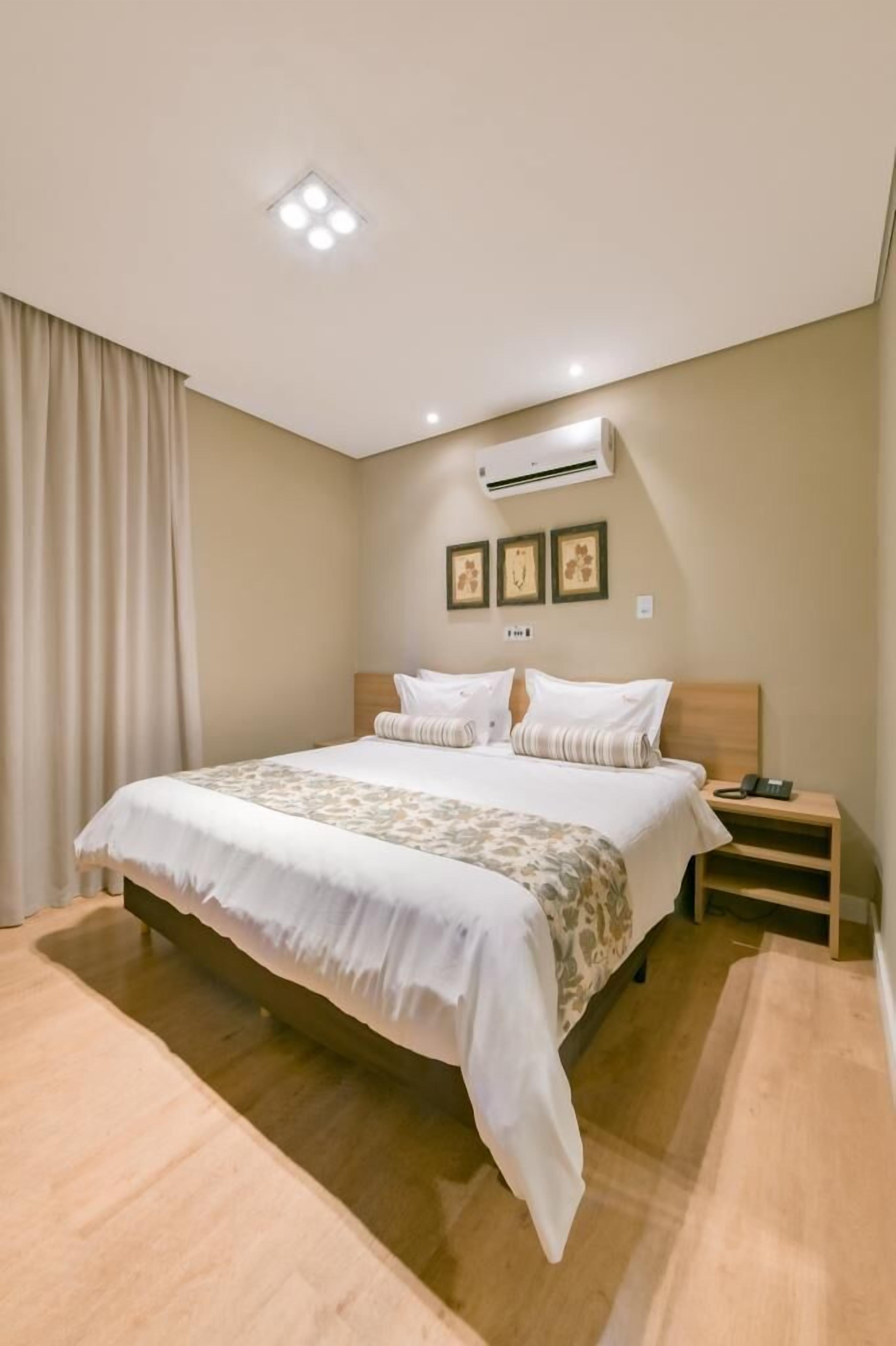 A neatly arranged bedroom with a large bed, a bedside table, an air conditioning unit, and a wall-mounted phone.